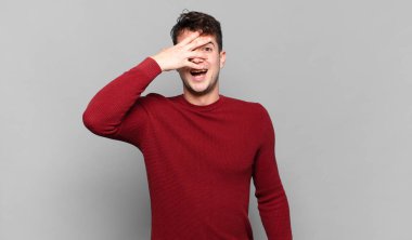 Genç adam şok olmuş, korkmuş ya da korkmuş görünüyor. Yüzü elle örtülmüş ve parmaklarının arasından gizlice bakıyor.