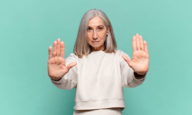 Orta yaşlı kadın ciddi görünüyor, mutsuz, kızgın ve hoşnutsuz giriş yasaklandı ya da her iki avuçta da dur diyor.