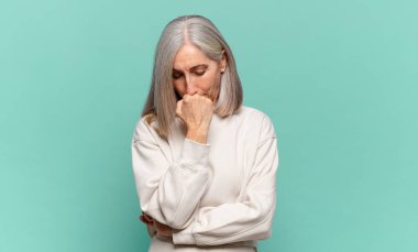 Orta yaşlı kadın ciddi, düşünceli ve endişeli, elleri çenesine bastırılmış bir şekilde yan bakıyor.