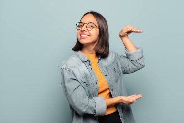 Genç İspanyol bir kadın iki eli yanda bir objeyi tutuyor fotokopi alanında, bir nesneyi gösteriyor, sunuyor ya da reklamını yapıyor.