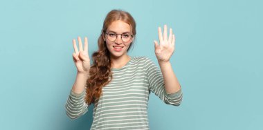 Sarışın, güzel bir kadın gülümsüyor ve arkadaş canlısı görünüyor, 8 ya da 8 numarayı gösteriyor, elleri önde, geriye doğru sayıyor.