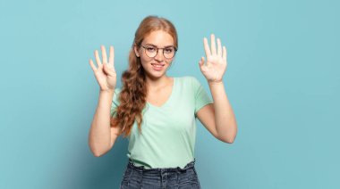 Sarışın, güzel bir kadın gülümsüyor ve arkadaş canlısı görünüyor. 9 ya da 9 numarayı gösteriyor. Eli önde, geriye doğru sayıyor.