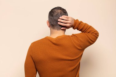 Yetişkin yakışıklı bir adam düşünüyor ya da şüphe ediyor, kafasını kaşıyor, kafası karışık ve kafası karışık hissediyor, geriye ya da arkaya bakıyor.