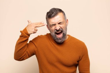 Yetişkin yakışıklı adam mutsuz ve stresli görünüyor, intihar jesti elle silah işareti yapıyor, kafasını işaret ediyor.