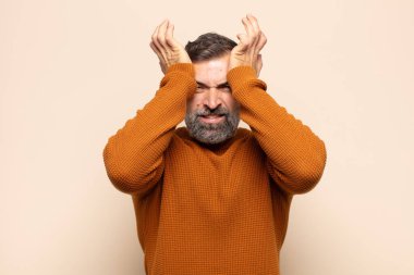 Yetişkin ve yakışıklı bir adam stresli ve endişeli, depresyonda ve hayal kırıklığına uğramış, iki elini de başa kaldırıyor.