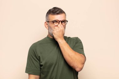 Yetişkin, yakışıklı bir adam iğrenç ve nahoş bir kokuyu koklamamak için burnunu tutuyor.