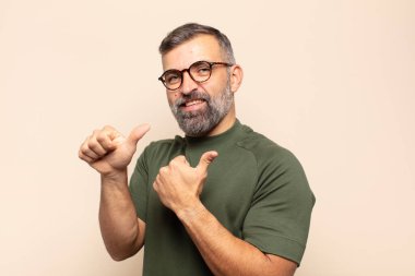 Yetişkin yakışıklı adam neşeli bir şekilde gülümsüyor ve yan taraftaki fotokopi alanını gösteriyor, mutlu ve tatmin olmuş hissediyor.