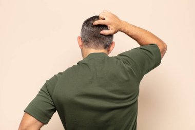 Yetişkin, yakışıklı bir adam bilgisiz ve kafası karışık, bir çözüm düşünüyor, eli kalçasında, diğeri kafasında, dikiz aynasından.