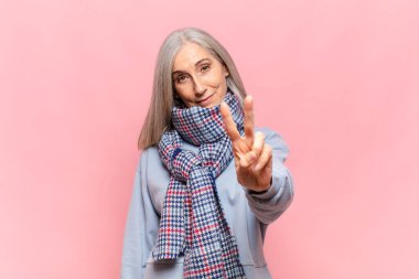 Orta yaşlı bir kadın gülümsüyor ve arkadaş canlısı görünüyor. İki ya da iki numarayı gösteriyor. Elleri önde, geriye doğru sayıyor.