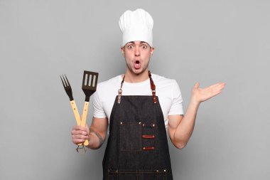 Genç adam şaşırmış ve şok olmuş görünüyor, çenesi düşmüş bir nesneyi elinde açık bir elle tutuyor.