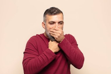 Yetişkin, yakışıklı bir adam boğazı ağrıyan ve grip belirtileri gösteren ağzı kapalı öksüren bir hasta.