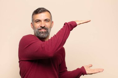 Yetişkin yakışıklı adam gülümsüyor, mutlu, pozitif ve tatmin olmuş hissediyor, fotokopi alanında nesne ya da konsept tutuyor ya da gösteriyor