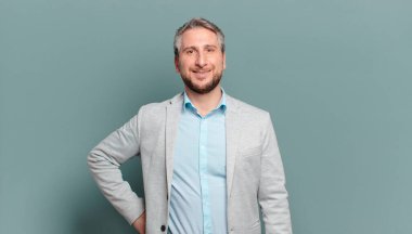 Yetişkin işadamı mutlu bir şekilde gülümsüyor. Kendine güvenen, olumlu, gururlu ve arkadaş canlısı bir tavırla.