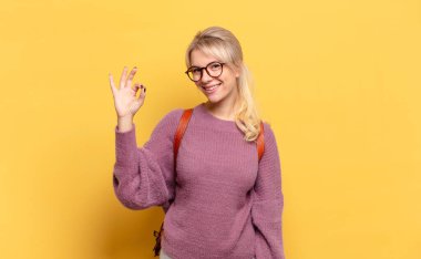 Sarışın kadın kendini mutlu, rahat ve tatmin olmuş hissediyor. Onayını iyi bir hareketle gösteriyor.