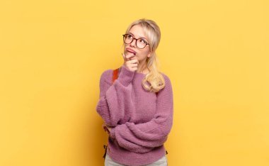 Sarışın kadın düşünüyor, kuşkulu ve şaşkın hissediyor, farklı seçenekleri var, hangi kararı vereceğini merak ediyor.