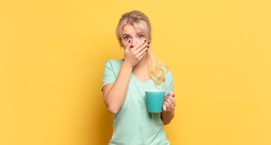 Sarışın kadın elleri ile ağzını kapatıyor, şok olmuş, şaşırmış bir ifadeyle, sır saklıyor ya da 