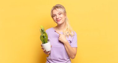 Sarışın kadın neşeyle gülümsüyor, mutlu hissediyor ve yan ve yukarı doğru işaret ediyor, fotokopi uzayındaki nesneleri gösteriyor.