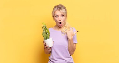 Sarışın kadın inançsızlıktan şaşkın şaşkın bakıyor, yan taraftaki objeyi işaret ediyor ve diyor ki: