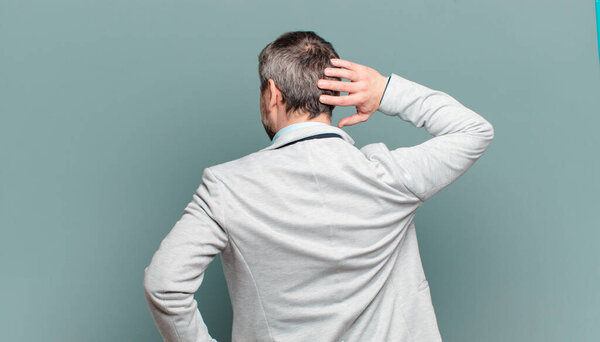 взрослый бизнесмен думает или сомневается, чешет голову, чувствует себя озадаченным и смущенным, вид сзади или сзади