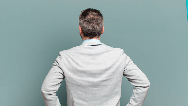 Взрослый бизнесмен чувствует себя смущенным или полным или сомнения и вопросы, интересно, с руками на бедрах, вид сзади