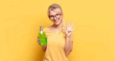 Sarışın kadın gülümsüyor ve arkadaş canlısı görünüyor, 4 ya da 4 numarayı gösteriyor, eli önde, geriye doğru sayıyor.