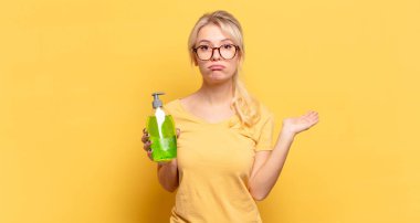 Sarışın kadın şaşırmış ve şoka uğramış görünüyor. Çenesi düşmüş ve eli açık bir objeyi tutuyor.