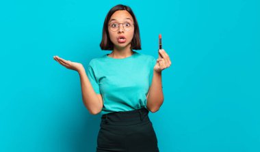 Genç İspanyol kadın şaşırmış ve şoka uğramış görünüyor, çenesi düşmüş, eli açık bir objeyi tutuyor.