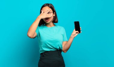 Genç İspanyol kadın şok olmuş, korkmuş ya da korkmuş görünüyor. Yüzü elle kaplanmış ve parmaklarının arasından gizlice bakıyor.