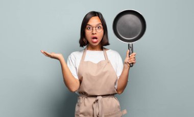 Genç İspanyol kadın şaşırmış ve şoka uğramış görünüyor, çenesi düşmüş, eli açık bir objeyi tutuyor.