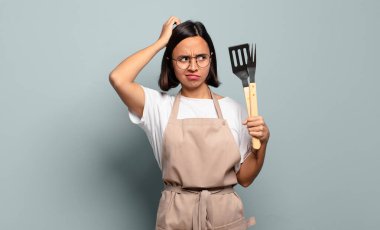 Genç İspanyol kadın şaşkın ve şaşkın hissediyor, kafasını kaşıyor ve yan tarafa bakıyor.