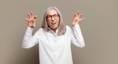 Yaşlı kadın panik ya da öfke içinde bağırıyor, şok olmuş, korkmuş ya da öfkeli, elleri başının yanında.