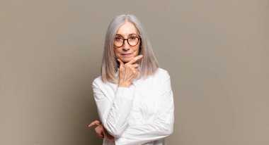 Son sınıf öğrencisi, ciddi, düşünceli ve güvensiz görünüyor. Bir kolu çapraz ve eli çene üzerinde, seçenekleri değerlendiriyor.