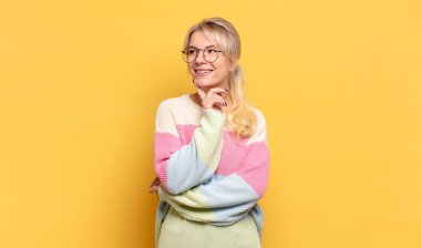 Sarışın kadın mutlu bir şekilde gülümsüyor ve hayal kuruyor ya da şüphe ediyor.