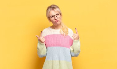 Kötü tavırlı sarışın kadın gururlu ve agresif görünüyor, yukarıyı işaret ediyor ya da elleriyle alay işareti yapıyor.