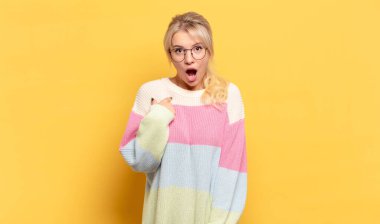 Şok olmuş ve ağzı açık, kendini işaret eden sarışın bir kadın.