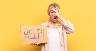 Sarışın kadın şok olmuş, korkmuş ya da korkmuş görünüyordu. Yüzü elle kaplıydı ve parmaklarının arasından bakıyordu.