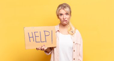 Sarışın kadın şaşkın ve şaşkın görünüyor. Sinirli bir hareketle dudağını ısırıyor. Sorunun cevabını bilmiyor.