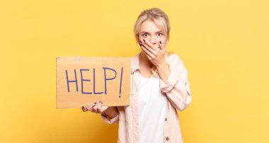 Sarışın kadın elleri ile ağzını kapatıyor, şok olmuş, şaşırmış bir ifadeyle, sır saklıyor ya da 