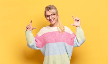 Sarışın bir kadın kendi gülüşünü çiziyor, iki eliyle, olumlu ve mutlu görünüyor, sağIık kavramı