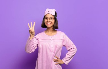 Genç İspanyol kadın gülümsüyor ve arkadaş canlısı görünüyor. Üç ya da üç numarayı gösteriyor. Elleri önde, geri sayıyor.