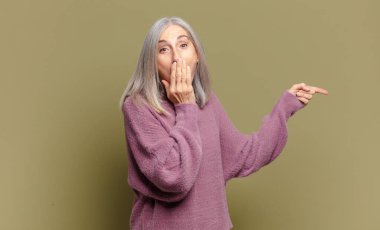 Son sınıf öğrencisi kadın kendini mutlu, şaşkın ve şaşırmış hissediyor. Ağzını eliyle kapatıyor ve yanal fotokopi alanını işaret ediyor.