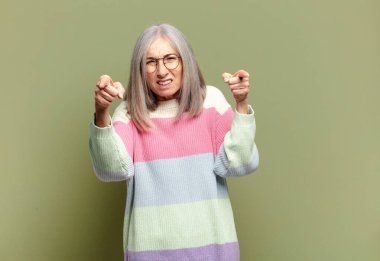 Kıdemli kadın kameraya hem parmaklarıyla hem de kızgın bir ifadeyle sana görevini yapmanı söylüyor.