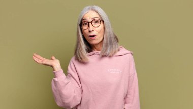 Son sınıf öğrencisi kadın şaşırmış ve şoka uğramış görünüyor. Çenesi düşmüş ve eli açık bir objeyi tutuyor.