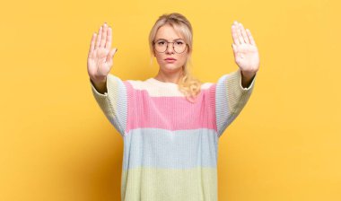 Sarışın kadın ciddi görünüyor, mutsuz, kızgın ve hoşnutsuz giriş yasaklandı ya da iki avucunun içinde de dur diyor.