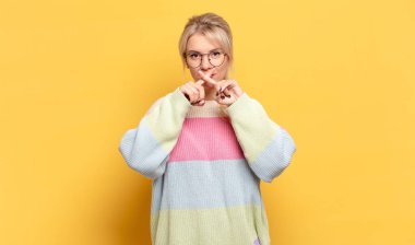 Sarışın kadın ciddi ve hoşnutsuz görünüyor. İki parmağın önde olsun, reddedilmek üzere, sessizlik istiyor.