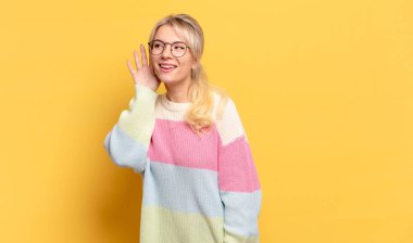 Sarışın kadın gülümsüyor, tuhaf bir şekilde yan tarafa bakıyor, dedikoduları dinlemeye ya da bir sırrı duymaya çalışıyor.