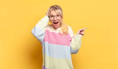 Sarışın kadın gülüyor, mutlu, pozitif ve şaşırmış görünüyor. Yan fotokopi alanını işaret eden harika bir fikrin farkına varıyor.