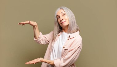 Bir objeyi iki eliyle fotokopi alanında tutan yaşlı bir kadın bir nesneyi gösteriyor, sunuyor ya da reklamını yapıyor.