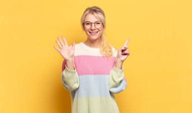 Sarışın kadın gülümsüyor ve arkadaş canlısı görünüyor, altı ya da altıncı numarayı gösteriyor, eli önde, geri sayıyor.