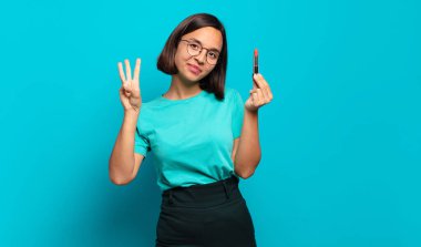 Genç İspanyol kadın gülümsüyor ve arkadaş canlısı görünüyor. Üç ya da üç numarayı gösteriyor. Elleri önde, geri sayıyor.